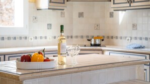 A kitchen with white cabinets, a tiled backsplash, a bowl of bell peppers, a bottle of white wine, and a wine glass. - Hillside Retreat in Roquebrun (Roquebrun)