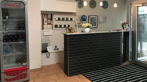 Zona de recepción con máquina expendedora de Coca-Cola, mostrador de recepción de ladrillo negro, un globo terráqueo y un reloj de pared.
