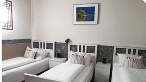 Habitación de hotel con tres camas individuales, cada una con cabecero blanco y almohadas a juego. En la pared, sobre las camas, hay un cuadro enmarcado con un paisaje.