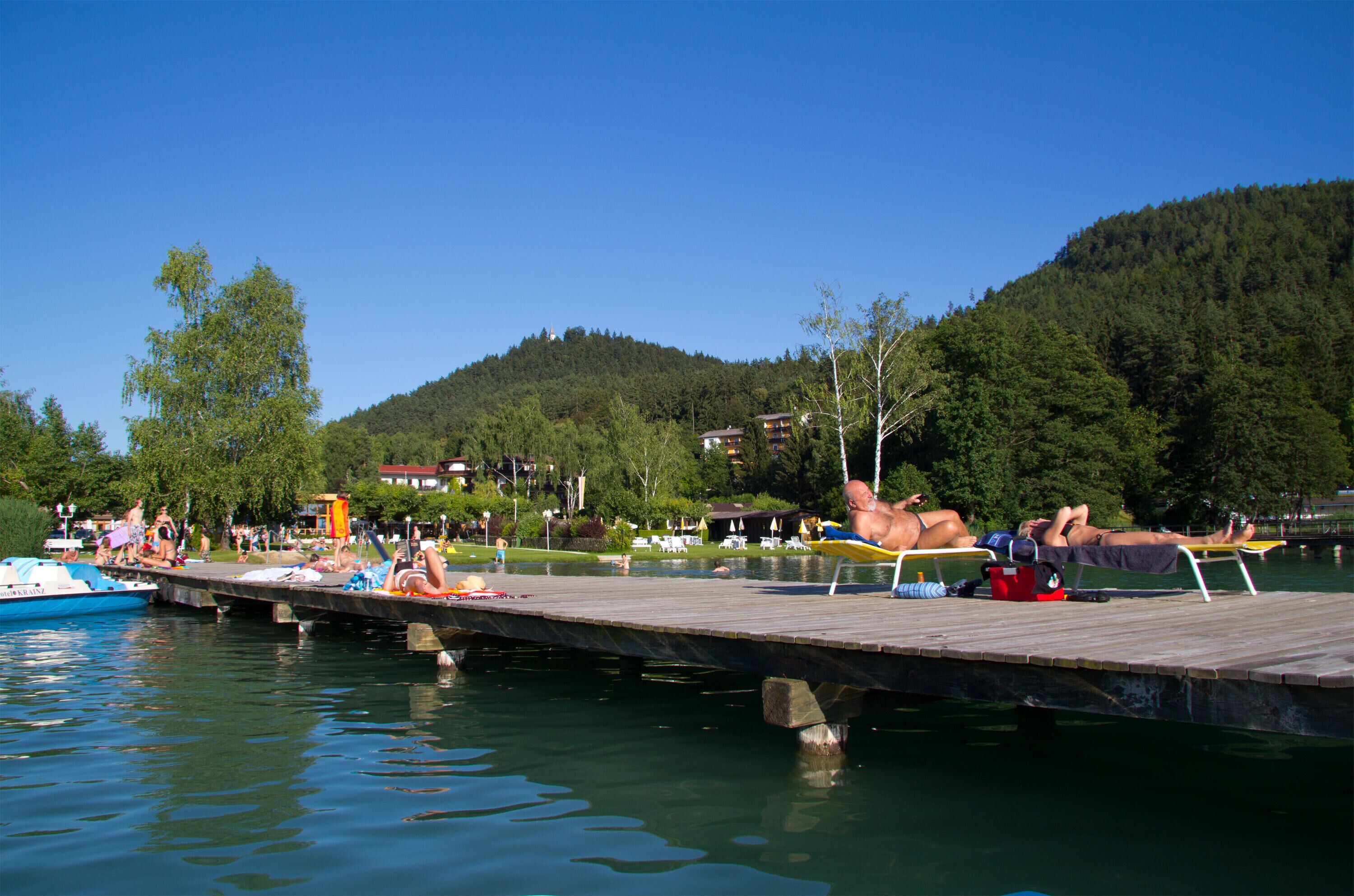 A wooden pier extending into a calm lake with people relaxing on it.