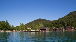 A lakeside village with wooden buildings, docks, and a forested hill in the background. - Modern apartment with large balcony on Lake Klopein (St. Kanzian)