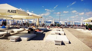 Un área de descanso frente a la playa con múltiples sillas y sillones blancos, protegidos por sombrillas blancas con el nombre 