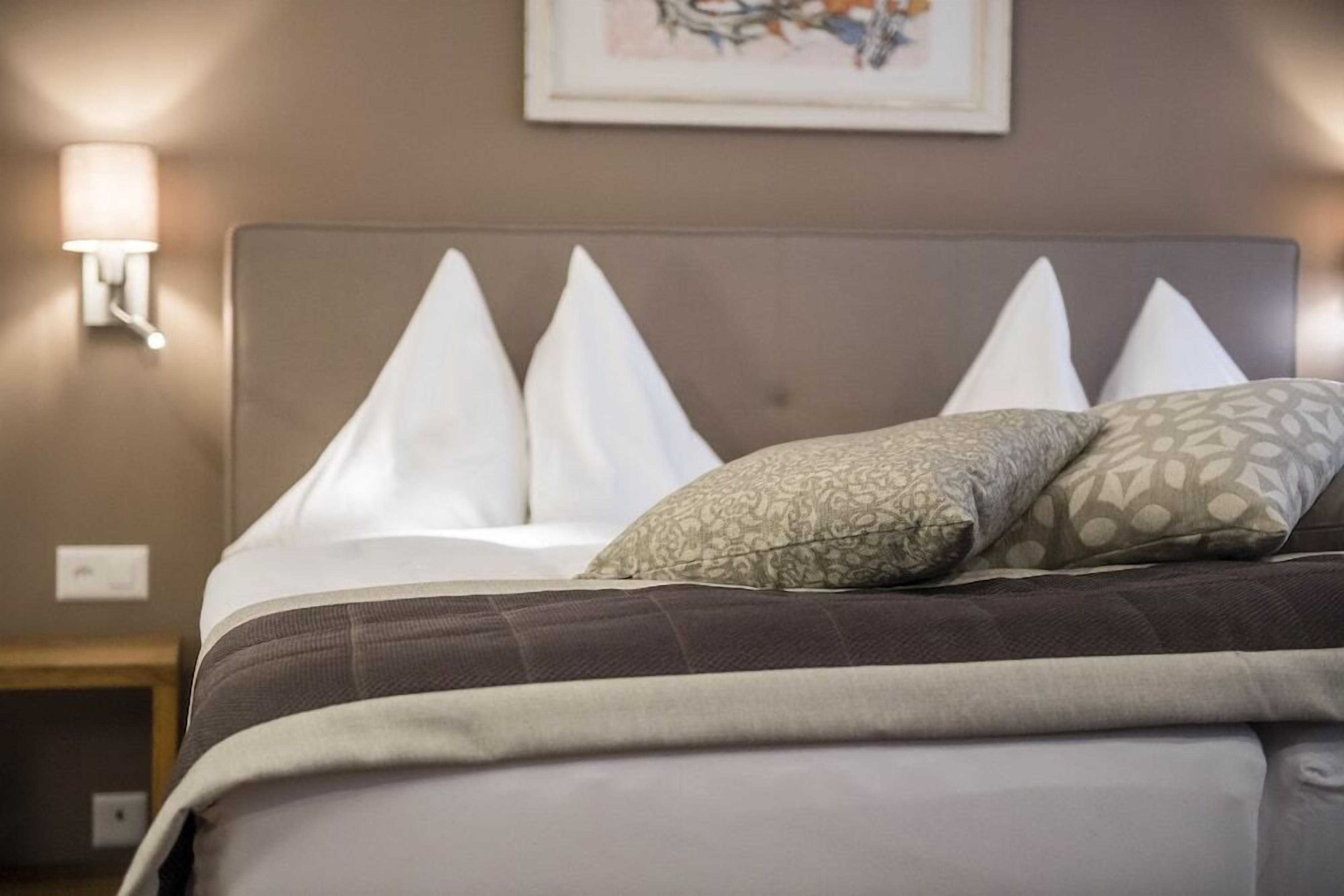 A neatly made bed with a headboard, white pillows, and a patterned pillow.