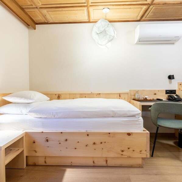 A wooden bed with a headboard, a bedside table with a lamp, and a chair. - Romantik Hotel Stern (Chur)