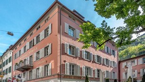 A hotel with a pink facade, multiple windows with shutters, and a balcony with plants. - Romantik Hotel Stern (Chur)