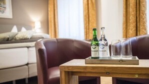 A wooden table with a bottle of Passugger Allega and two glasses, a leather armchair, and a white sofa in a room with a window and curtains. - Romantik Hotel Stern (Chur)