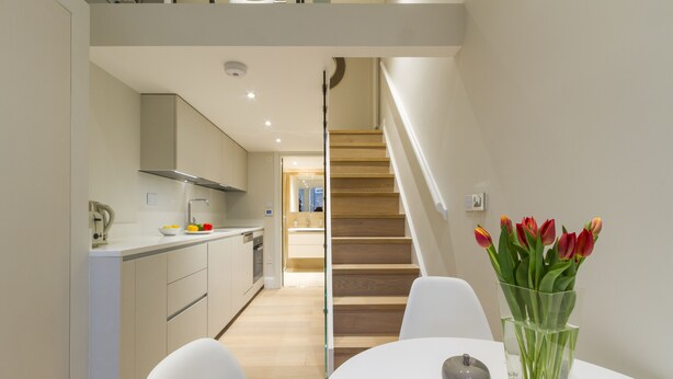 Eine moderne Küche mit weißen Schränken, einer Holztreppe und einem Essbereich mit weißem Tisch und Stühlen.