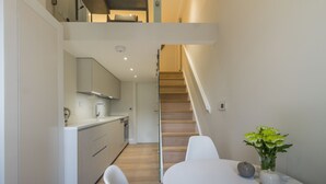 Eine moderne Küche mit weißen Schränken, einer Holztreppe und einer Essecke mit weißen Stühlen und einem Tisch.