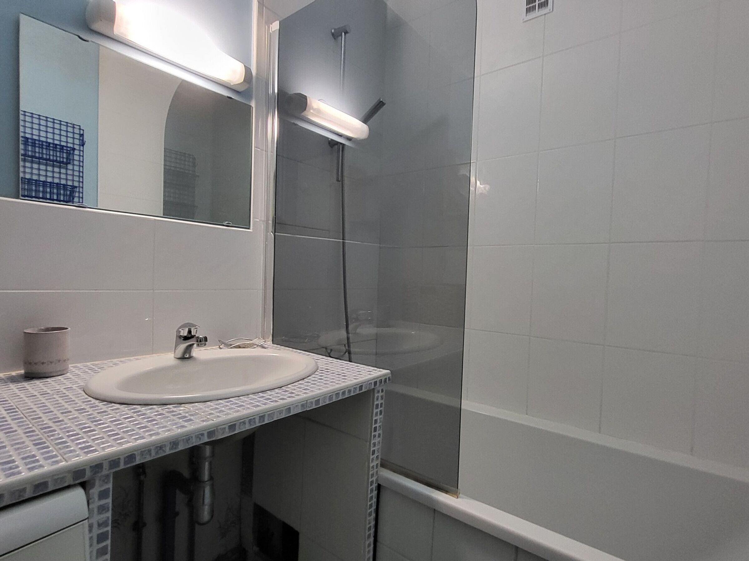 A bathroom with a white sink, a mirror, and a shower area.
