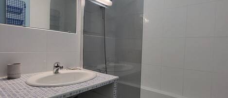 A bathroom with a white sink, a mirror, and a shower area.