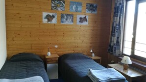 Una habitación con dos camas, paredes de madera y una ventana con cortinas.