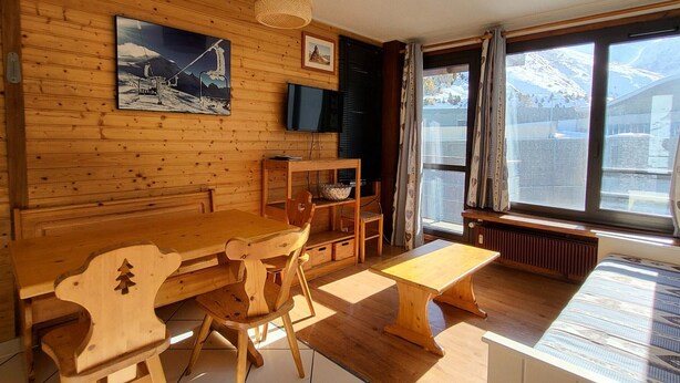 Un interior de madera con una mesa de comedor, sillas, un televisor y un ventanal con vista a la montaña.