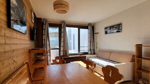 Una habitación acogedora con paredes y mesa de madera. Hay una ventana con cortinas, un sofá y una lámpara.
