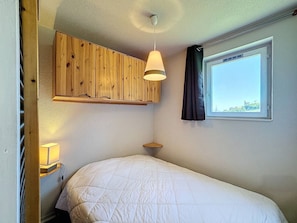 Una camera da letto con un letto, un armadietto in legno, una finestra con tende e una lampada a sospensione.