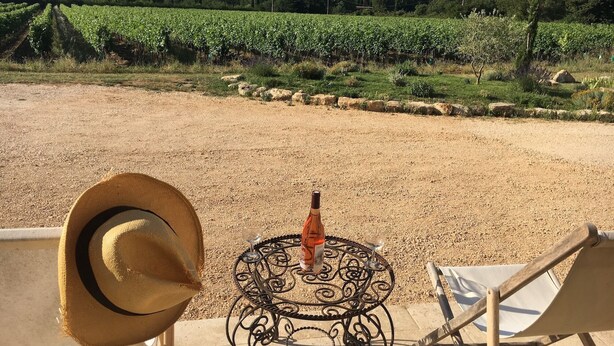 Vista de un viñedo desde una terraza con una mesa, un sombrero y una silla.