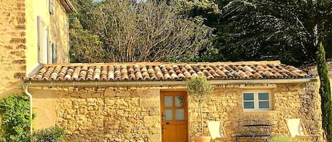 A stone building with a tiled roof, a wooden door, and a window.