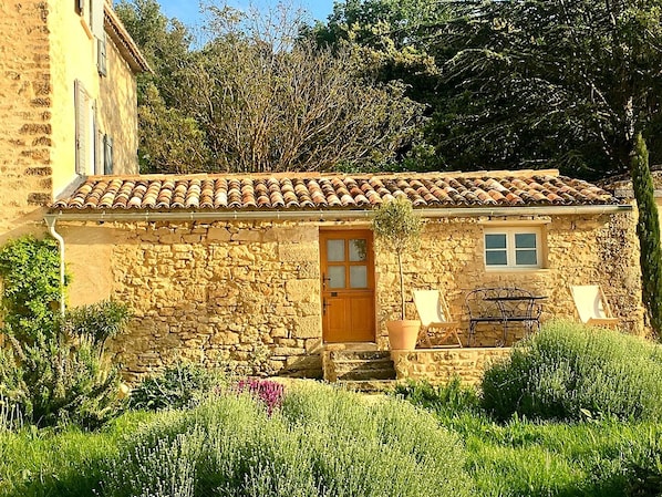 A stone building with a tiled roof, a wooden door, and a window.