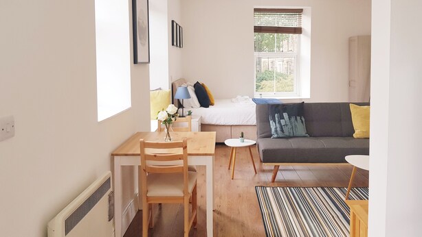 Un salon moderne comprenant un canapé, une table à manger avec des chaises, une petite table ronde et une fenêtre avec des stores.