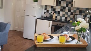 Une cuisine moderne avec des appareils électroménagers blancs, un dosseret à carreaux et un plateau de petit-déjeuner avec des croissants et du jus d’orange.
