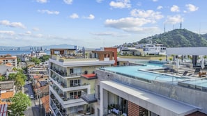 A modern residential building with a rooftop pool, multiple balconies, and a view of the sea.