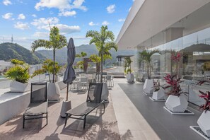 A rooftop terrace with outdoor seating, potted plants, and a view of the cityscape. - Rooftop Pool & Bar + Gym | Romantic Zone Stay (Puerto Vallarta)