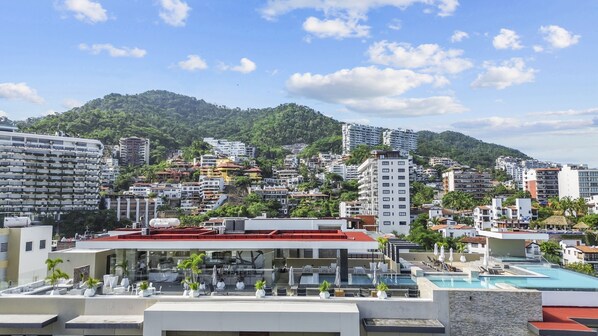 A hotel with a rooftop pool, surrounded by a cityscape and a mountain. - Rooftop Pool & Bar + Gym | Romantic Zone Stay (Puerto Vallarta)
