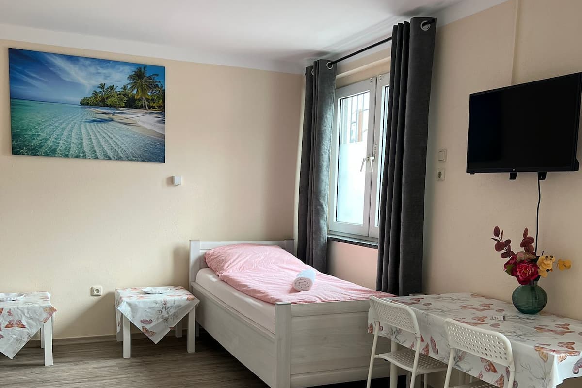 A bedroom with a bed, a table with chairs, a TV, and a painting of a beach.