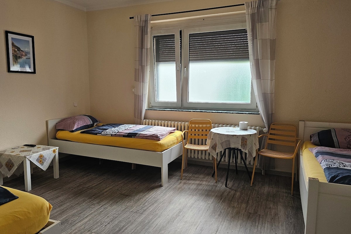 A bedroom with a bed, a small table, a chair, and a window with curtains.