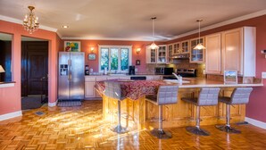 Una cocina con suelo de madera en patrón de espiga, una isla central con taburetes de bar, electrodomésticos de acero inoxidable e iluminación colgante.