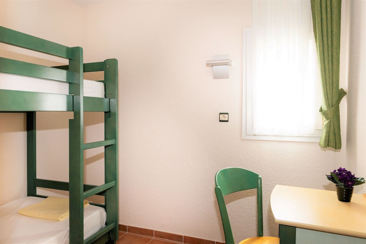 Una cama individual superpuesta con estructura verde, una silla, una mesita y una ventana con cortina.