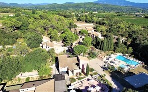 Vue aérienne d’un complexe hôtelier doté d’une piscine, entouré d’une végétation luxuriante et d’un paysage vallonné.