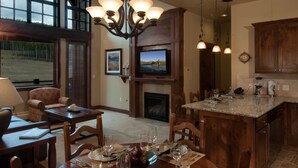 A dining area with a fireplace, a television mounted above it, and a kitchen with wooden cabinets and a granite countertop. - Ski in/Ski out room on Peak 7 for Presidents Day Week! (Breckenridge)