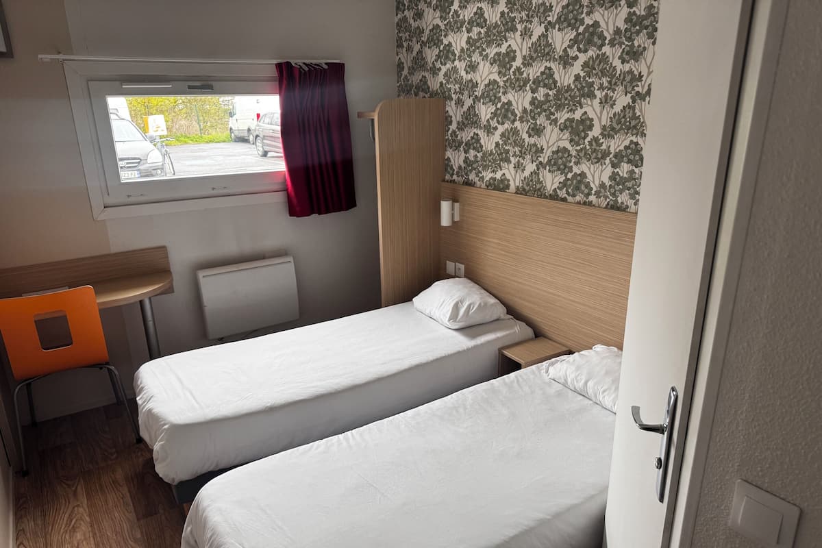 A bedroom with two beds, a desk, and a window with a view of the outside.