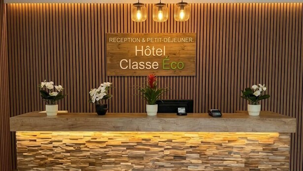 A reception desk with a wooden finish, a sign above it, and three pendant lights. - Hôtel Classe Eco Reims Tinqueux (Tinqueux)