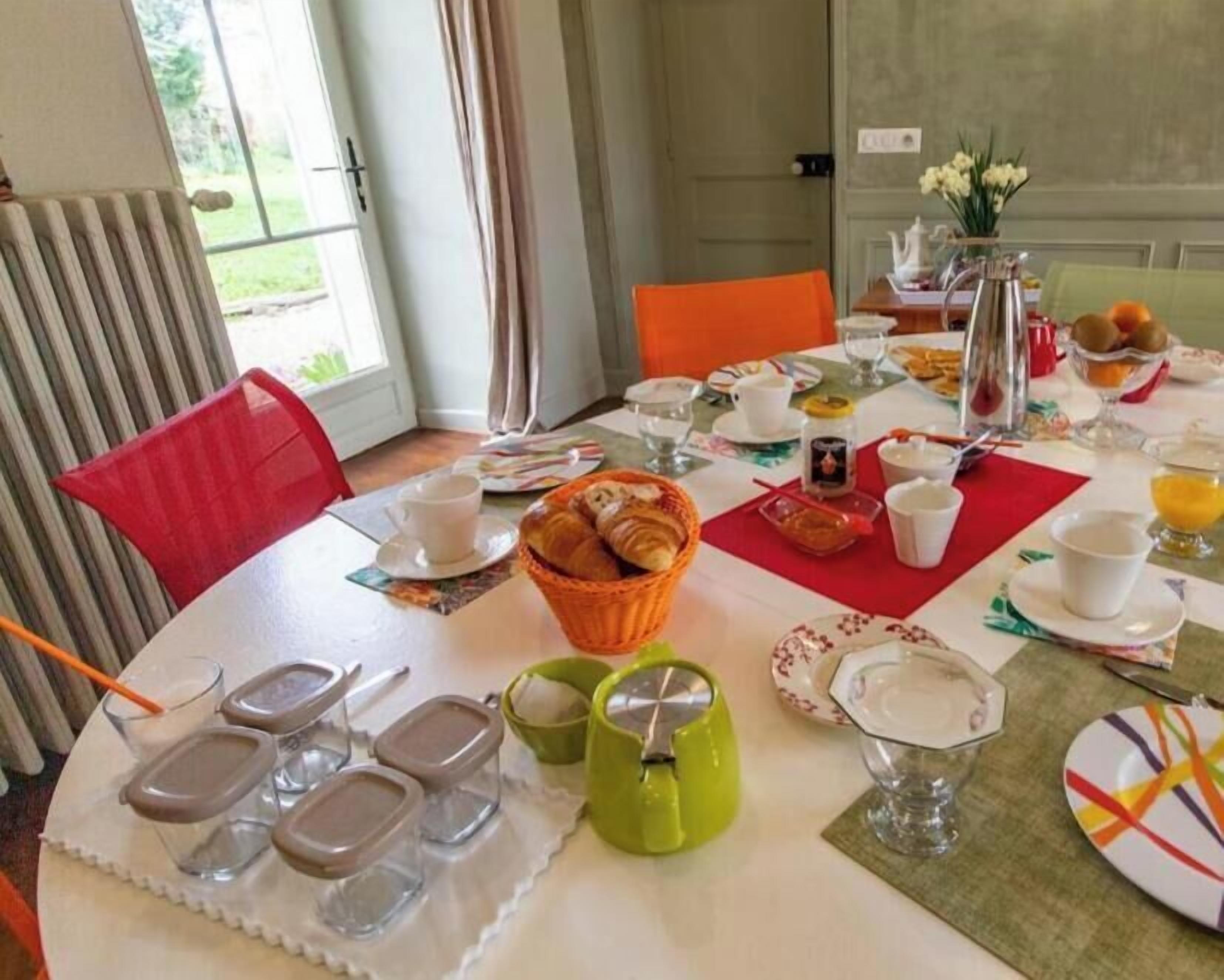 A breakfast table set with various dishes, cups, and a basket of croissants.