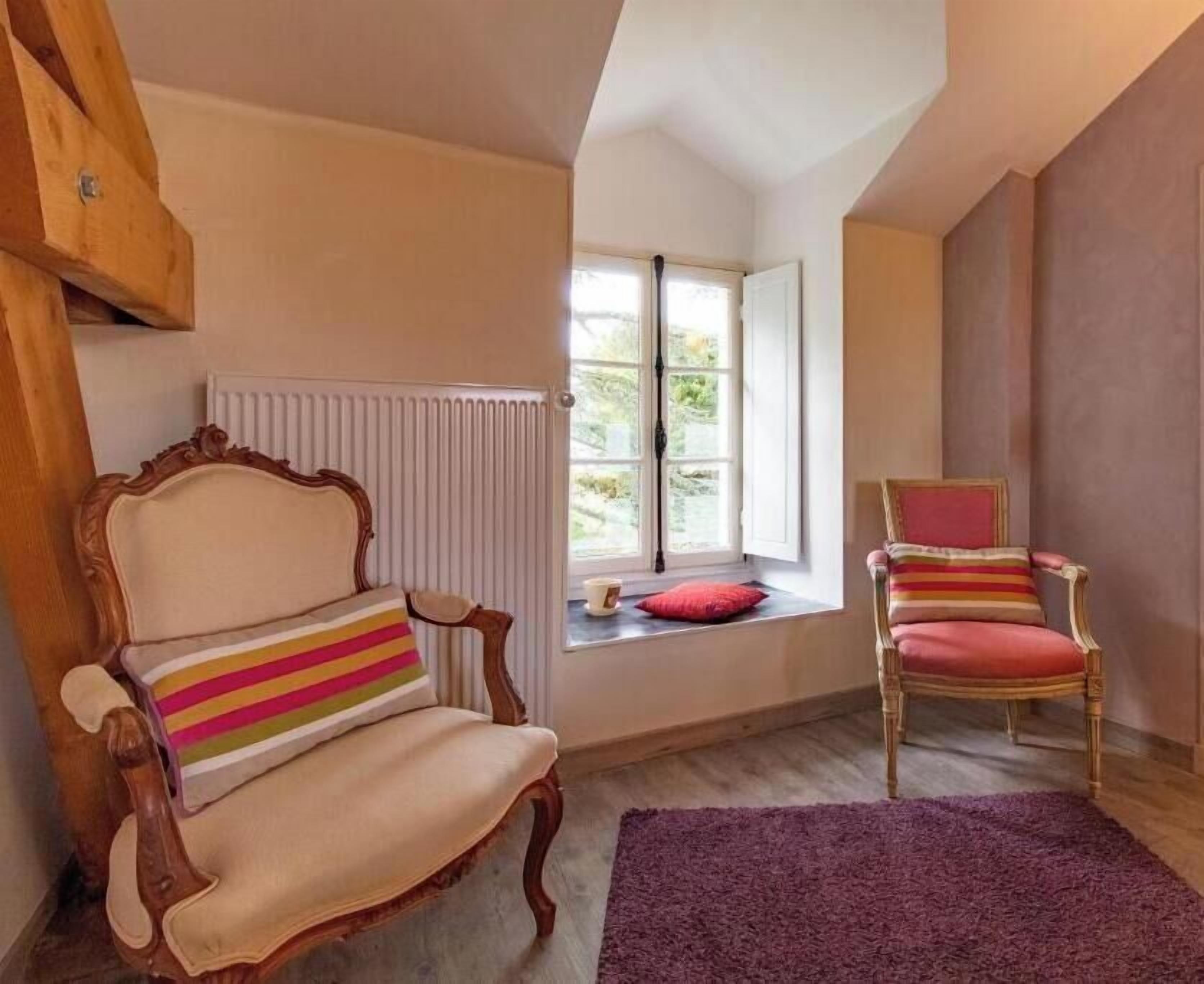 A room with a wooden chair, a cushioned chair with a striped pillow, a window with a view, and a radiator.