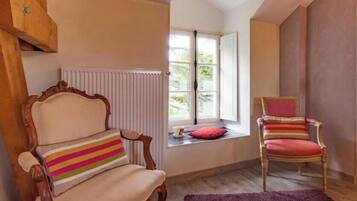 A room with a wooden chair, a cushioned chair with a striped pillow, a window with a view, and a radiator.