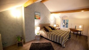 Un dormitorio con cama, mesitas de noche, una ventana y una puerta.