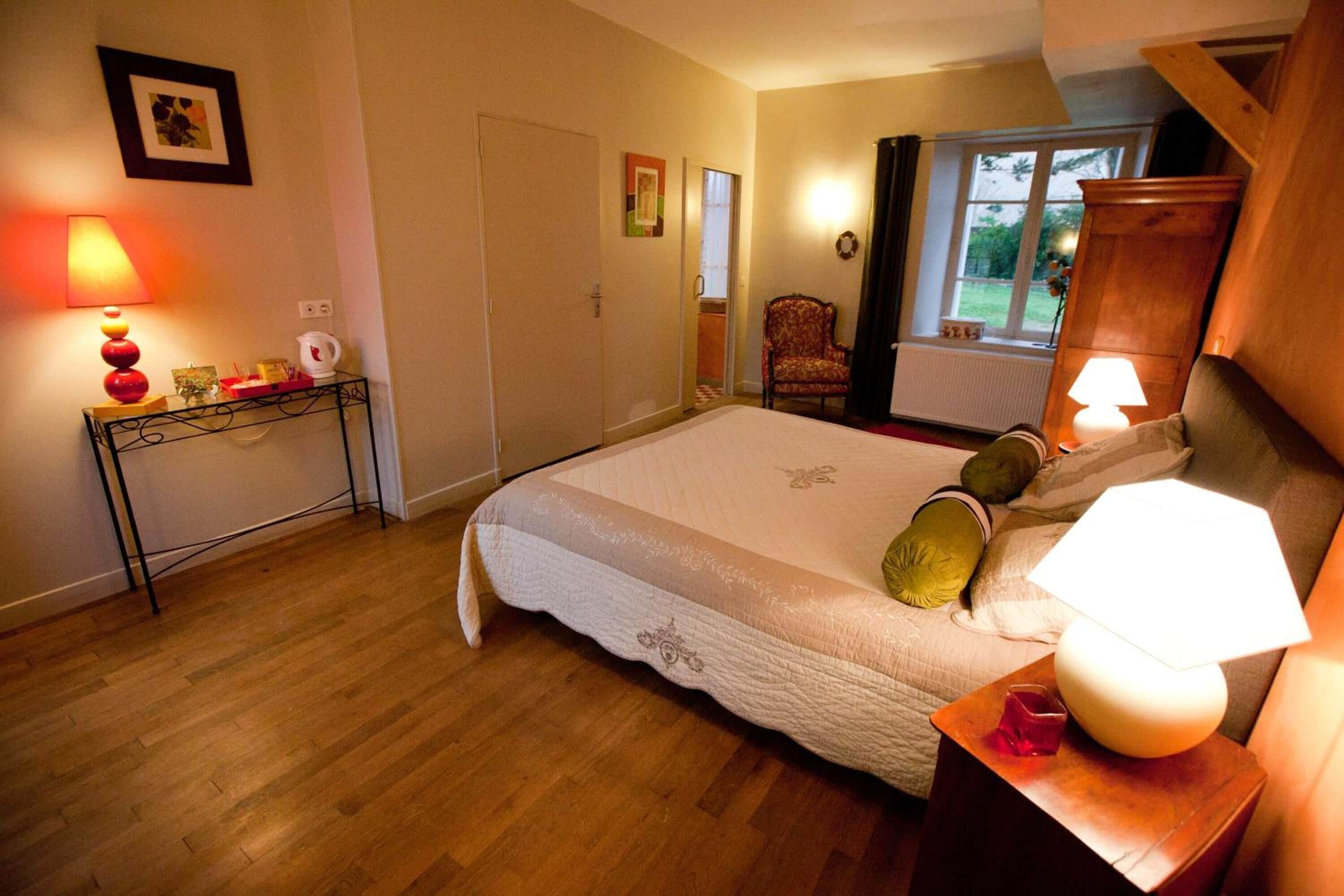 Een keurig opgemaakt slaapkamer met een bed, bedlampjes, een klein tafeltje met een lamp en een stoel.