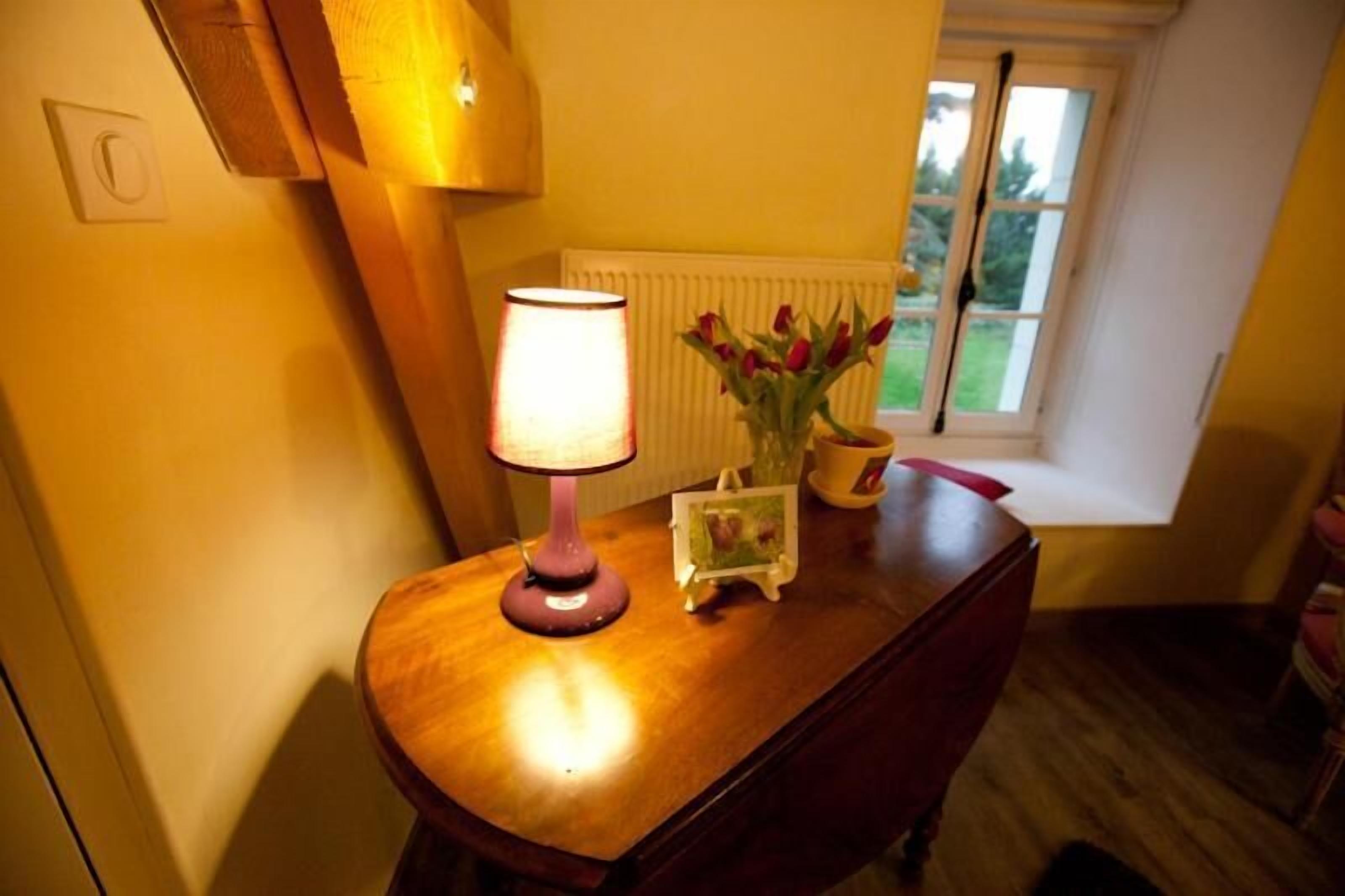 A wooden table with a lamp, a vase with red flowers, and a framed picture.