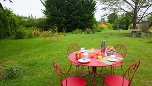 Mesa metálica roja al aire libre con sillas, rodeada de follaje y árboles.