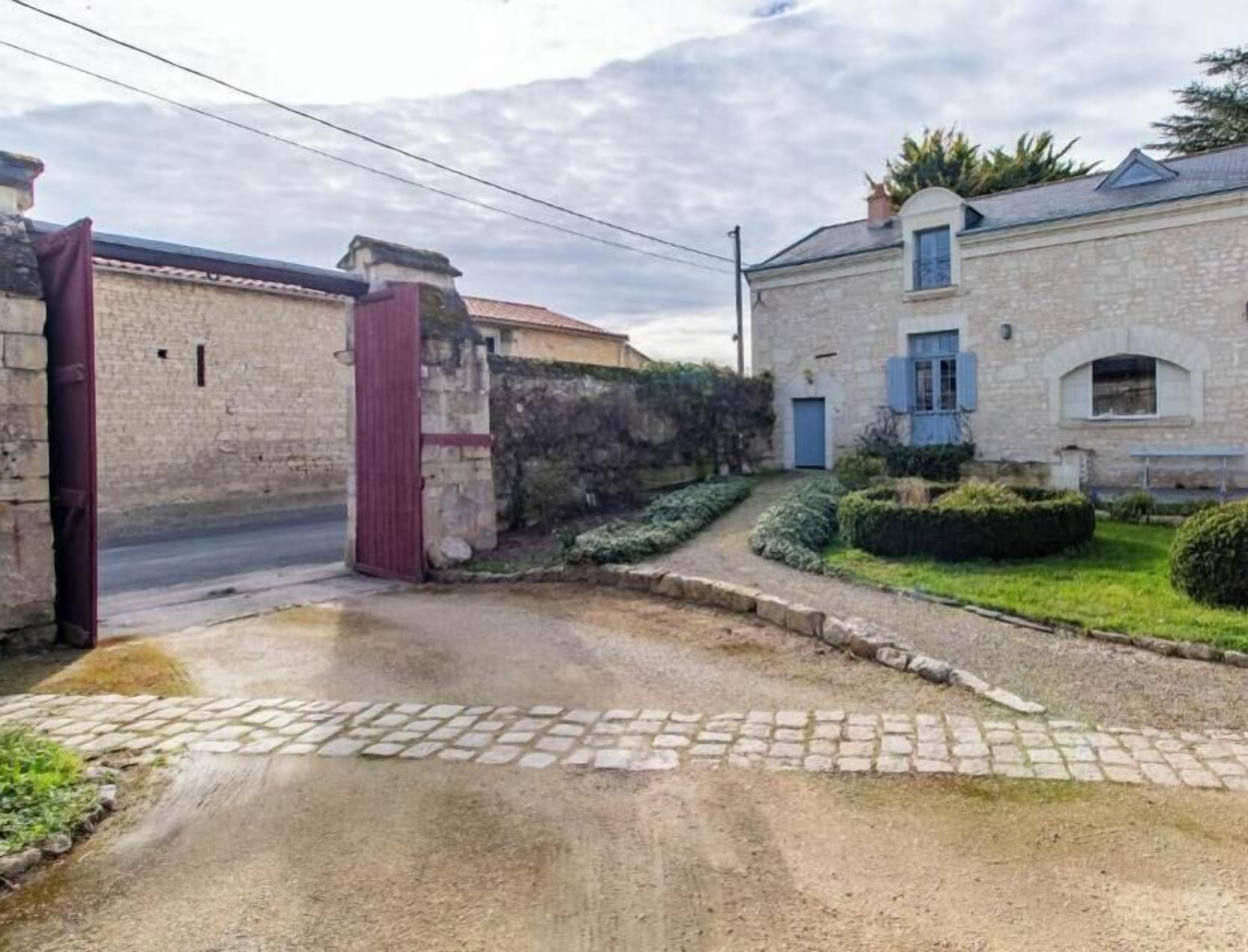 A gated entrance to a property with a paved driveway leading to a stone building.