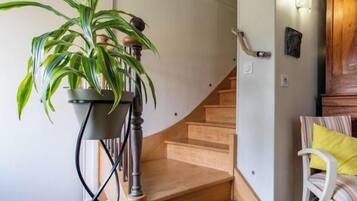 Un escalier avec une finition en bois, un pot de fleurs sur la gauche et une chaise avec un coussin jaune sur la droite.