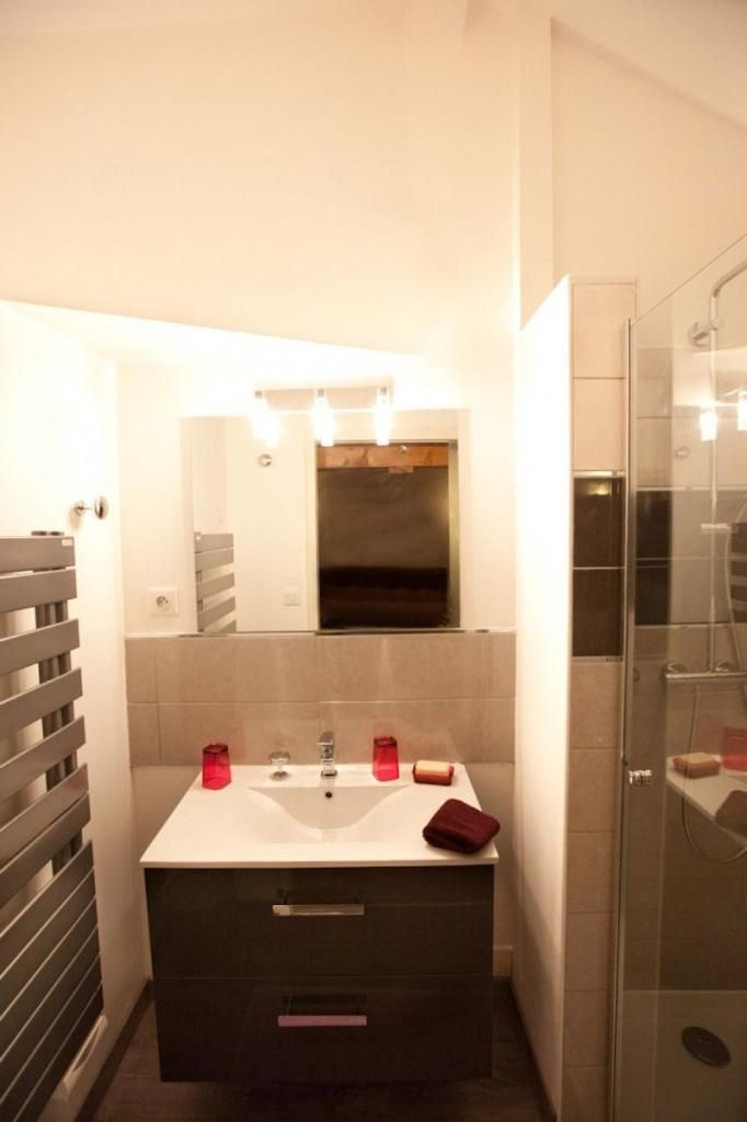Ein modernes Badezimmer mit einem weißen Waschtisch, einer Duschkabine aus Glas und einem Spiegel über dem Waschbecken.