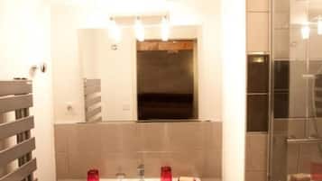 Ein modernes Badezimmer mit einem weißen Waschtisch, einer Duschkabine aus Glas und einem Spiegel über dem Waschbecken.