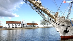 A large ship docked by a waterfront with buildings in the background. - Hotel Utkiek (Greifswald)