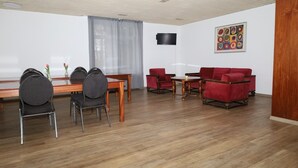 A room with a wooden floor, a dining table with chairs, a TV mounted on the wall, and a red sofa. - Pension Highway 3 Sennestadt-Bielefeld (Bielefeld)
