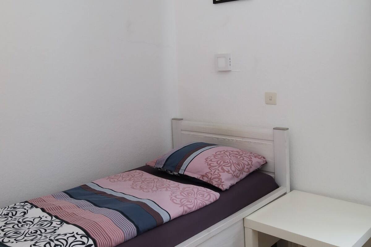 A single bed with a patterned bedspread, a bedside table, and a framed picture on the wall.