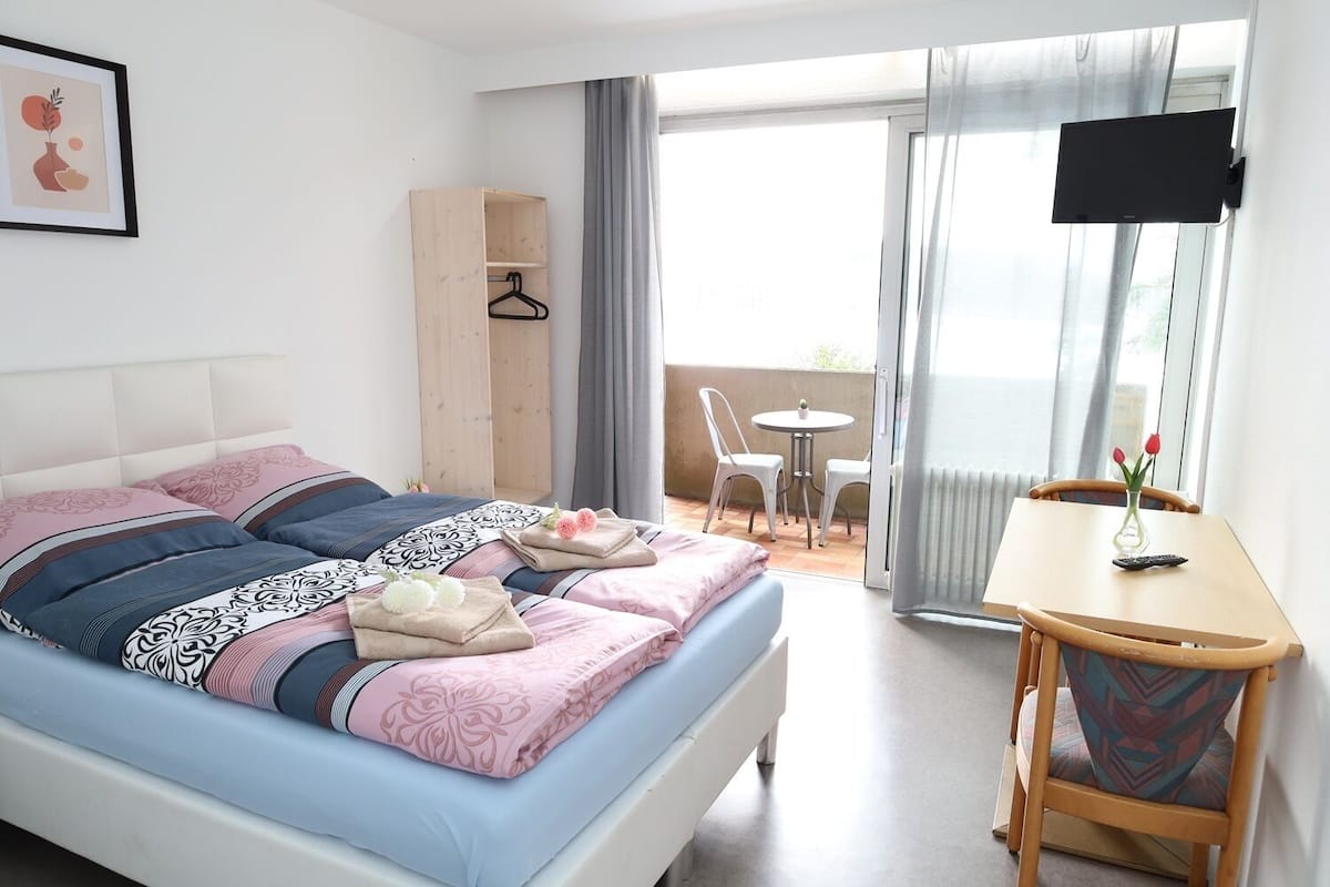 A bedroom with a bed, bedside table, and a view of the balcony.