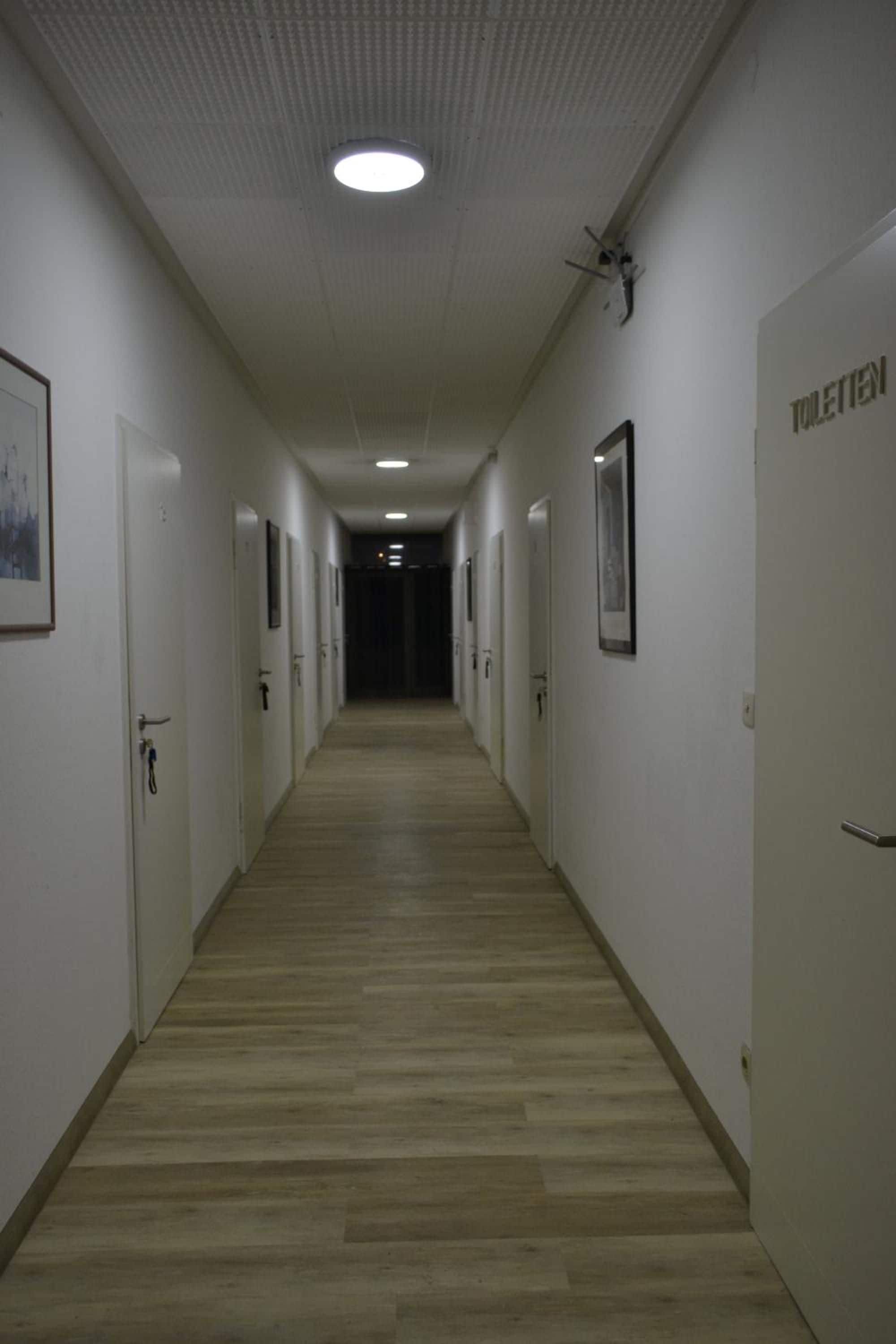 Un pasillo largo y estrecho con puertas a ambos lados, que conduce a una zona oscura al final.